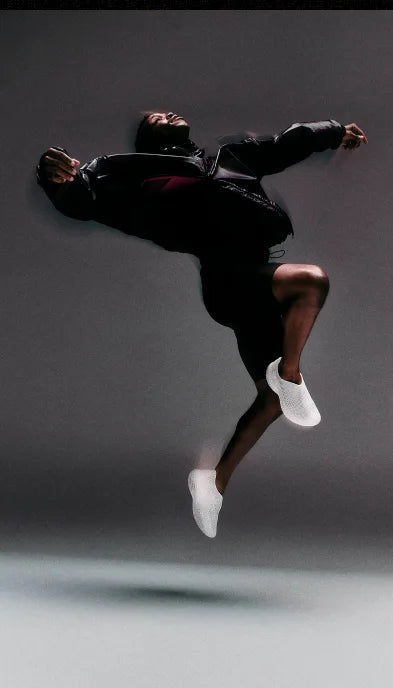 Person in black outfit and white shoes jumping against a dark background