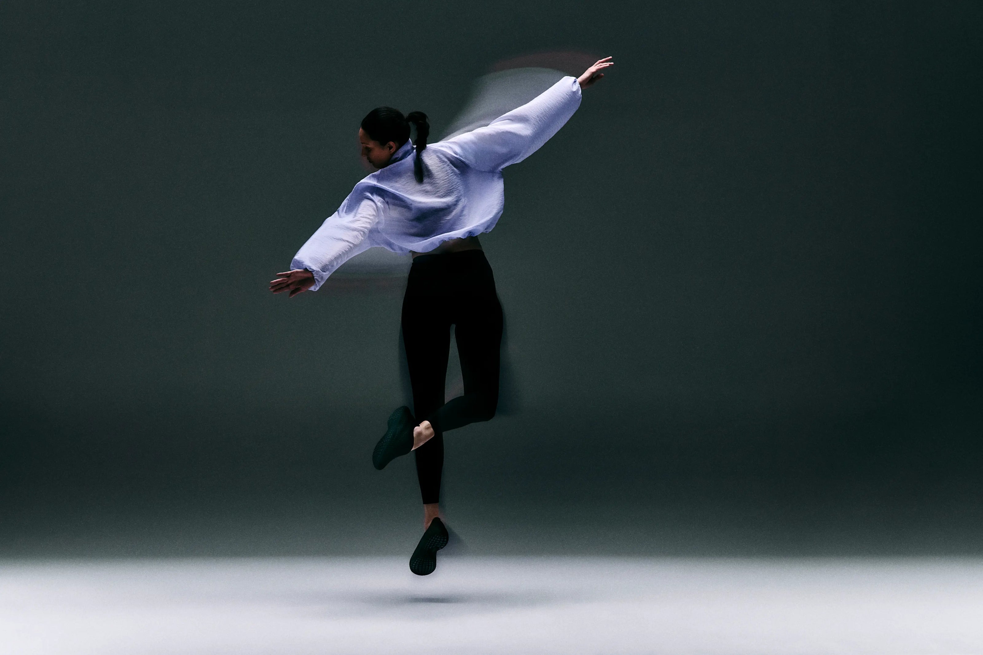 Dancer in a white shirt and black pants performing a jump against a dark background