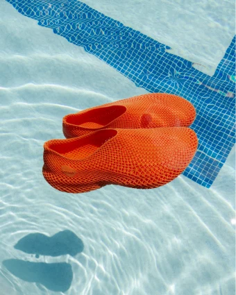 Orange mesh shoes floating in a pool with blue tiled edge.