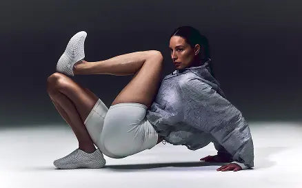 Woman in light gray outfit with white socks posing against a dark background